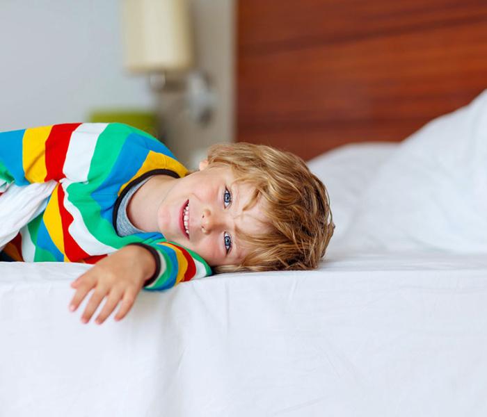 Bambino felice in pigiama a righe colorate, sdraiato su un letto bianco.